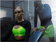 Charger l'image dans la galerie, Femme et homme avec écouteurs dans la salle de sport. Soutien-gorge sport vert. Vêtements noirs.
