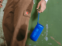 Charger l'image dans la galerie, Une personne tient un haut-parleur bleu, portant un pantalon cargo marron.
