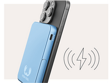 Charger l&#39;image dans la galerie, Un smartphone charge une batterie externe bleue, avec un symbole de charge sans fil.
