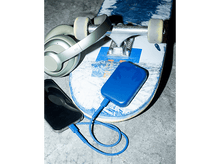 Charger l'image dans la galerie, Batterie externe bleue sur une planche à roulettes. Casque et téléphone connectés. Fond en béton.
