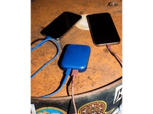 Charger l'image dans la galerie, Deux téléphones se chargeant à partir d'une batterie externe bleue. Fond en métal rouillé.
