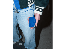 Charger l'image dans la galerie, Personne tenant une batterie externe bleue, connectée à un cordon. Jean bleu, fond sombre.
