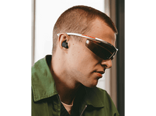 Charger l'image dans la galerie, Un homme portant des lunettes de soleil Prada et une veste verte, avec des écouteurs.
