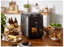 Charger l&#39;image dans la galerie, Friteuse à air noire avec de la nourriture à l&#39;intérieur et autour sur une table en bois.

