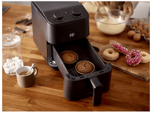 Charger l&#39;image dans la galerie, Une friteuse à air avec deux cupcakes à l&#39;intérieur et des donuts sur le côté, avec des ingrédients sur la table en bois.
