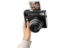 Charger l&#39;image dans la galerie, Une personne tient un appareil photo instantané noir et une photo imprimée en sort.
