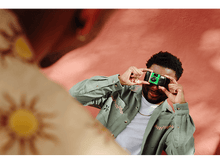 Charger l&#39;image dans la galerie, Un homme prenant une photo avec un appareil photo QuickSnap, avec une personne floue au premier plan.
