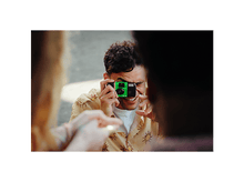 Charger l&#39;image dans la galerie, Homme prenant photo avec un appareil QuickSnap, une autre personne au premier plan.
