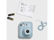 Charger l&#39;image dans la galerie, Appareil photo bleu Instax Mini 12 avec accessoires : piles, sangle et manuel, sur fond blanc.
