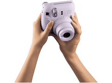 Charger l&#39;image dans la galerie, Une personne tenant un appareil photo Instax 12 lavande. Les mains tiennent l&#39;appareil photo à hauteur des yeux, prêt à prendre une photo.
