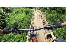 Charger l'image dans la galerie, Vue à la première personne d'un cycliste sur un pont en bois au-dessus d'un ruisseau. La végétation verte entoure le pont.
