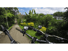 Charger l'image dans la galerie, Deux VTT avec des GoPros montés sur le guidon sur une route. Arbres et lac en arrière-plan.
