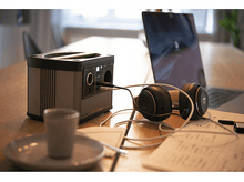 Charger l&#39;image dans la galerie, Une centrale électrique avec un casque et un ordinateur portable sur une table en bois. Il y a une tasse et un carnet.
