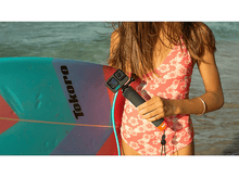 Charger l'image dans la galerie, Une personne tenant une GoPro sur un bâton près de l'océan, avec une planche de surf en vue.
