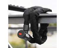 Charger l&#39;image dans la galerie, Un antivol à chaîne noir fixé à une barre métallique. Le cadenas a un bouton rouge.

