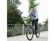 Charger l&#39;image dans la galerie, Une personne faisant du vélo sur un sentier pavé, portant un casque et un sweat à capuche gris.
