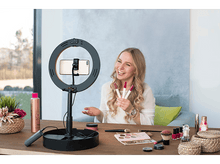 Charger l&#39;image dans la galerie, Une femme filmant avec une lampe annulaire, tenant des rouges à lèvres, avec du maquillage et des accessoires sur une table.

