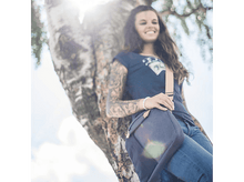 Charger l&#39;image dans la galerie, Une femme s&#39;appuie contre un arbre, souriante, portant un t-shirt et un jean.
