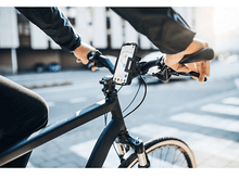 Charger l&#39;image dans la galerie, Personne faisant du vélo avec un téléphone monté sur le guidon, affichant une carte. Scène extérieure ensoleillée.
