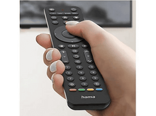 Charger l&#39;image dans la galerie, Une main tient une télécommande noire avec de nombreux boutons. La télécommande porte la marque &#39;hama&#39;. Une télévision est en arrière-plan.
