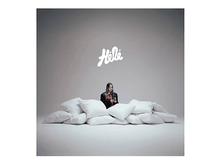 Charger l'image dans la galerie, Une femme en blazer est assise derrière des oreillers. Le mot 'Hola' est au-dessus d'elle. Le fond est gris clair.
