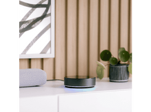 Charger l&#39;image dans la galerie, Un hub intelligent avec un anneau lumineux brillant à côté d&#39;un haut-parleur et d&#39;une plante.
