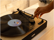 Charger l&#39;image dans la galerie, Une main place l&#39;aiguille sur un disque vinyle sur une platine vinyle en bois.
