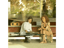 Charger l&#39;image dans la galerie, Deux personnes assises sur un canapé regardant une platine. Un haut-parleur est également visible.
