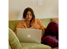 Charger l&#39;image dans la galerie, Femme utilisant un ordinateur portable sur un canapé, avec un tableau sur le mur derrière elle.
