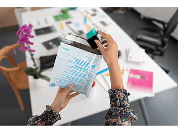 Mains tenant une cartouche d'encre HP au-dessus d'une enveloppe ouverte sur table.