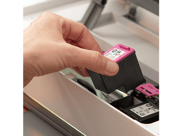 Une main tenant une cartouche d'encre noire et rose, prête à être insérée dans une imprimante.