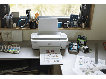 Imprimante blanche imprimant un motif floral avec des cartouches d'encre sur une table avec des outils.