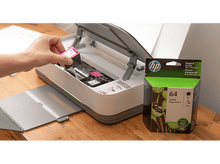 Charger l&#39;image dans la galerie, Main insérant une cartouche d&#39;encre magenta dans une imprimante HP. Boîte d&#39;encre verte et noire présente.
