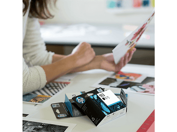 Femme tenant une impression, avec des cartouches d'encre HP sur une table, entourée d'autres impressions.