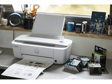 Charger l&#39;image dans la galerie, Une imprimante HP blanche avec du papier, des cartouches d&#39;encre et une fenêtre en arrière-plan.
