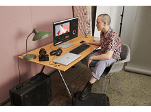 Charger l&#39;image dans la galerie, Personne à un bureau avec un ordinateur, un appareil photo et un casque. Logiciel de montage affiché à l&#39;écran.
