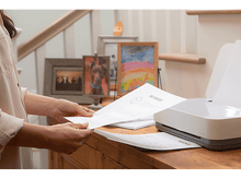 Charger l&#39;image dans la galerie, Femme tenant des papiers près d&#39;une imprimante sur une surface en bois.
