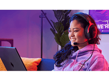 Charger l&#39;image dans la galerie, Femme portant un casque, souriante, assise devant un ordinateur portable avec un fond violet.
