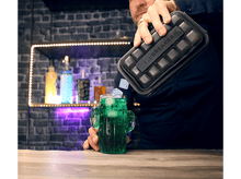 Charger l&#39;image dans la galerie, Homme versant des glaçons d&#39;un récipient noir dans un verre cactus vert.
