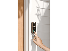 Charger l&#39;image dans la galerie, Une main appuyant sur un bouton vert sur une sonnette argentée fixée à une porte blanche.
