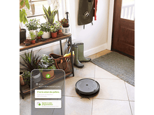 Charger l&#39;image dans la galerie, Un aspirateur robot sur un sol carrelé. Il y a des plantes et une porte en arrière-plan.
