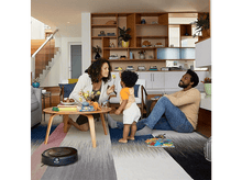 Charger l&#39;image dans la galerie, Famille dans le salon avec un aspirateur robot et des jouets sur la table.

