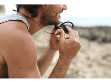 Charger l&#39;image dans la galerie, Homme tenant des écouteurs sans fil noirs avec un arrière-plan de littoral.
