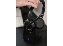 Charger l&#39;image dans la galerie, Un casque noir sur un socle de chargement noir, tenu par une main. Le socle a une lumière bleue.
