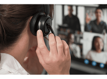 Charger l&#39;image dans la galerie, Femme portant un casque, participant à un appel vidéo. L&#39;écran montre une conférence téléphonique floue.
