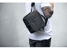 Charger l&#39;image dans la galerie, Personne portant un sac messager gris avec une sangle noire, sur un tee-shirt blanc.
