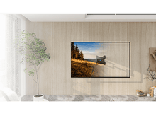 Charger l&#39;image dans la galerie, Un téléviseur est monté sur un mur en bois. Un arbre et une chaise sont à gauche du téléviseur.
