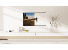 Charger l&#39;image dans la galerie, TV monté sur mur blanc, image de paysage à l&#39;écran, étagère blanche avec livres et fleurs.
