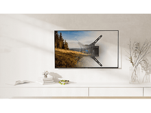 Charger l&#39;image dans la galerie, TV monté sur mur blanc, montre un paysage, avec un livre et des fleurs.
