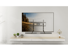 Charger l&#39;image dans la galerie, Un support TV noir installé sur un mur blanc. Un téléviseur est monté dessus, avec une barre de son en dessous.
